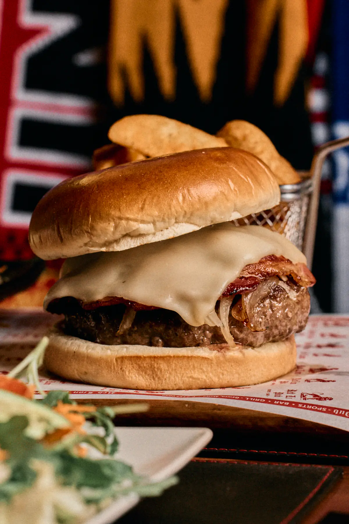A bacon cheeseburger with melted cheese and onions, potato wedges in a basket behind