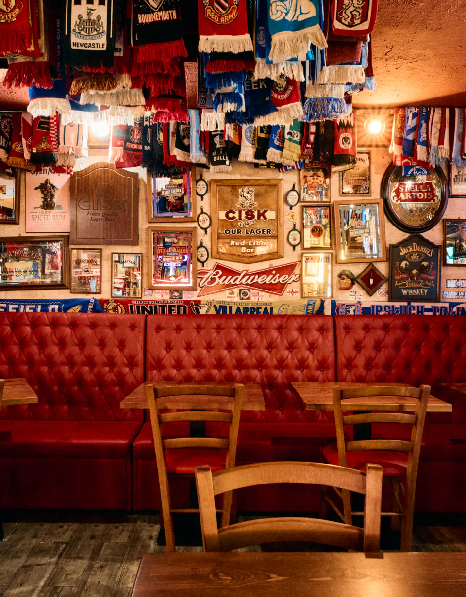 Red leather booths under a wall of framed beer signs and a ceiling hung with football scarves