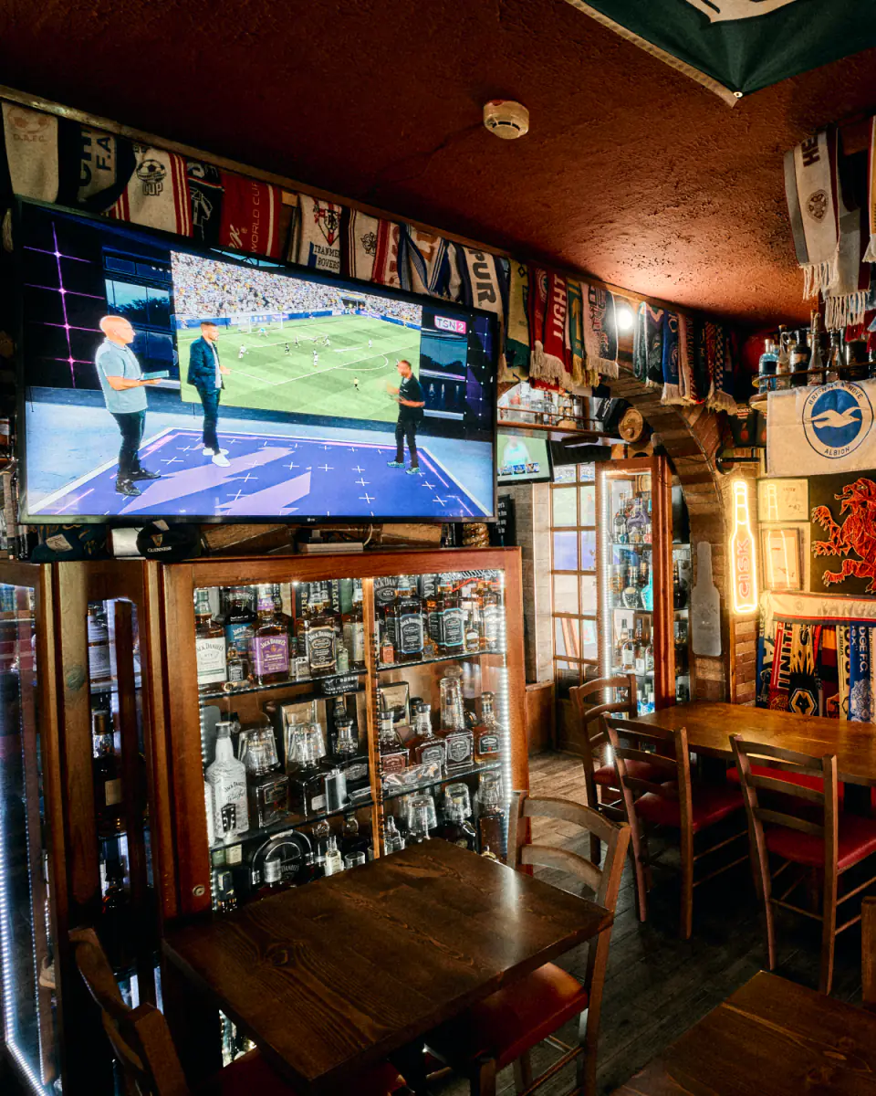 The bar, with football on the big screen above the whiskey cabinet and scarves along the ceiling
